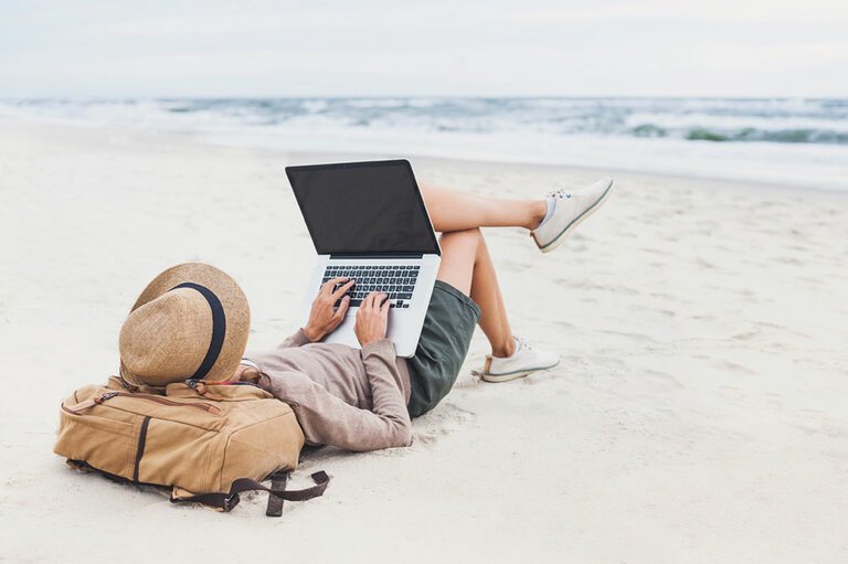 Liegende Person mit Laptop am Strand