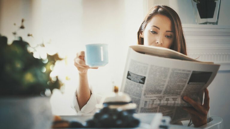 Junge Frau mit Zeitung und Kaffeebecher